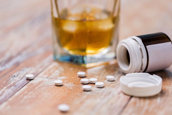 glass of liquor next to bottle of pills - pills spilling out - alcohol and opioids