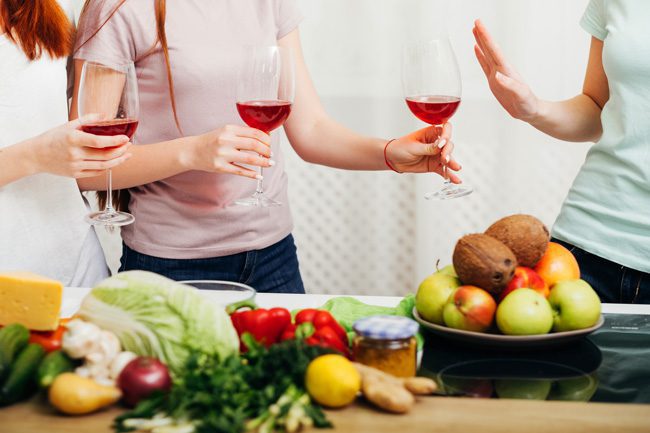 women drinking wine in kitchen - woman offers friend wine and she declines - social
