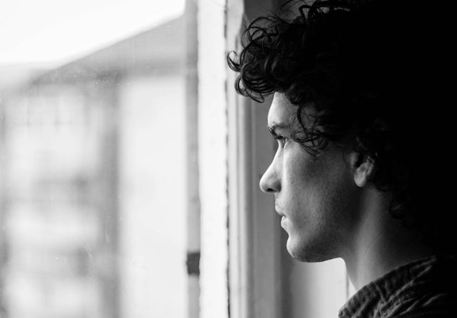 black and white - young man looking out window - weather